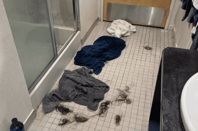 Gemeinschaftsbadboden mit Haaren und nassen Handtüchern neben der Duschkabine