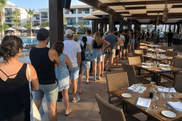 Terraza del restaurante de la piscina con mesas vacías y una larga cola de huéspedes esperando